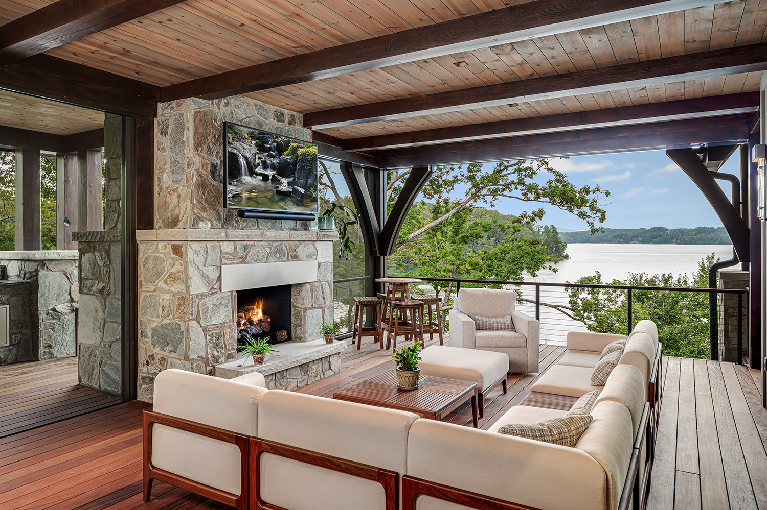 Lakefront outdoor living room with stone fireplace, white upholstered seating, and open water views — exterior design by Mac & Morgan Interiors, Lake Keowee SC