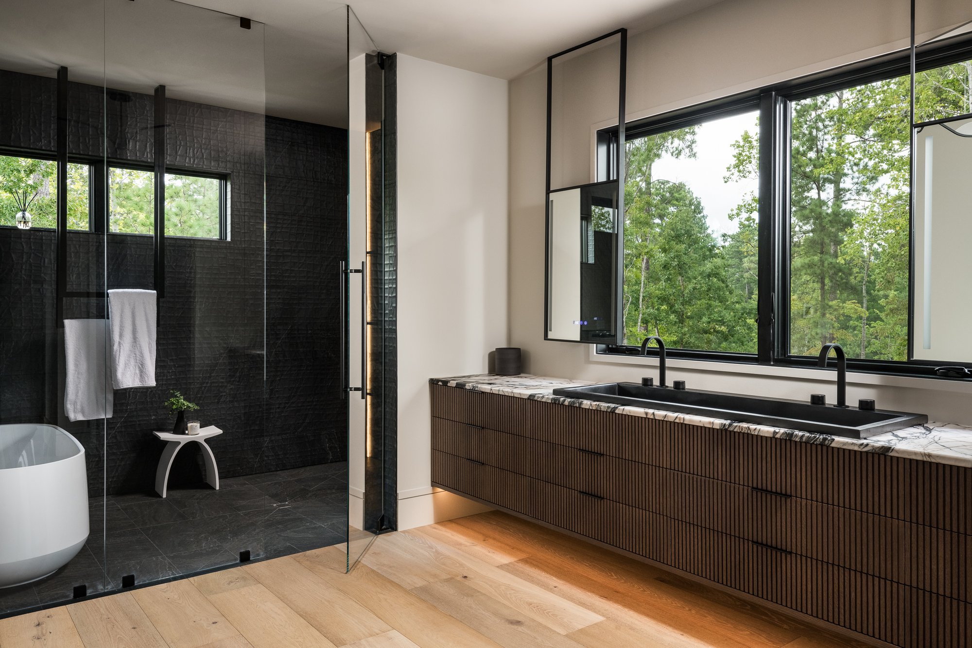 Luxury primary bathroom with black marble tile, glass walk-in shower, freestanding soaking tub, and floating wood vanity — Mac & Morgan Interiors, Upstate SC