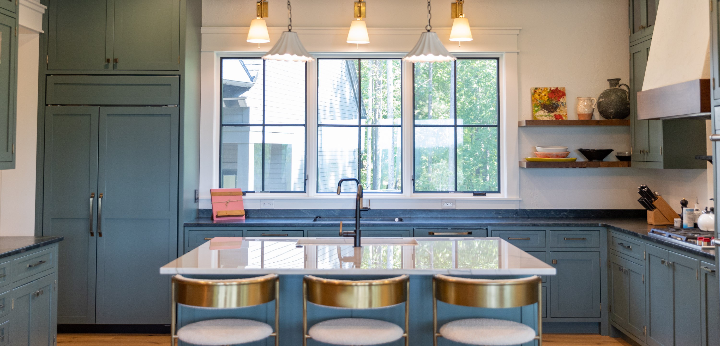 Kitchen with sage green cabinetry, quartz island, brass bar stools, and steel-framed windows — interior design by Mac & Morgan Interiors, Western NC