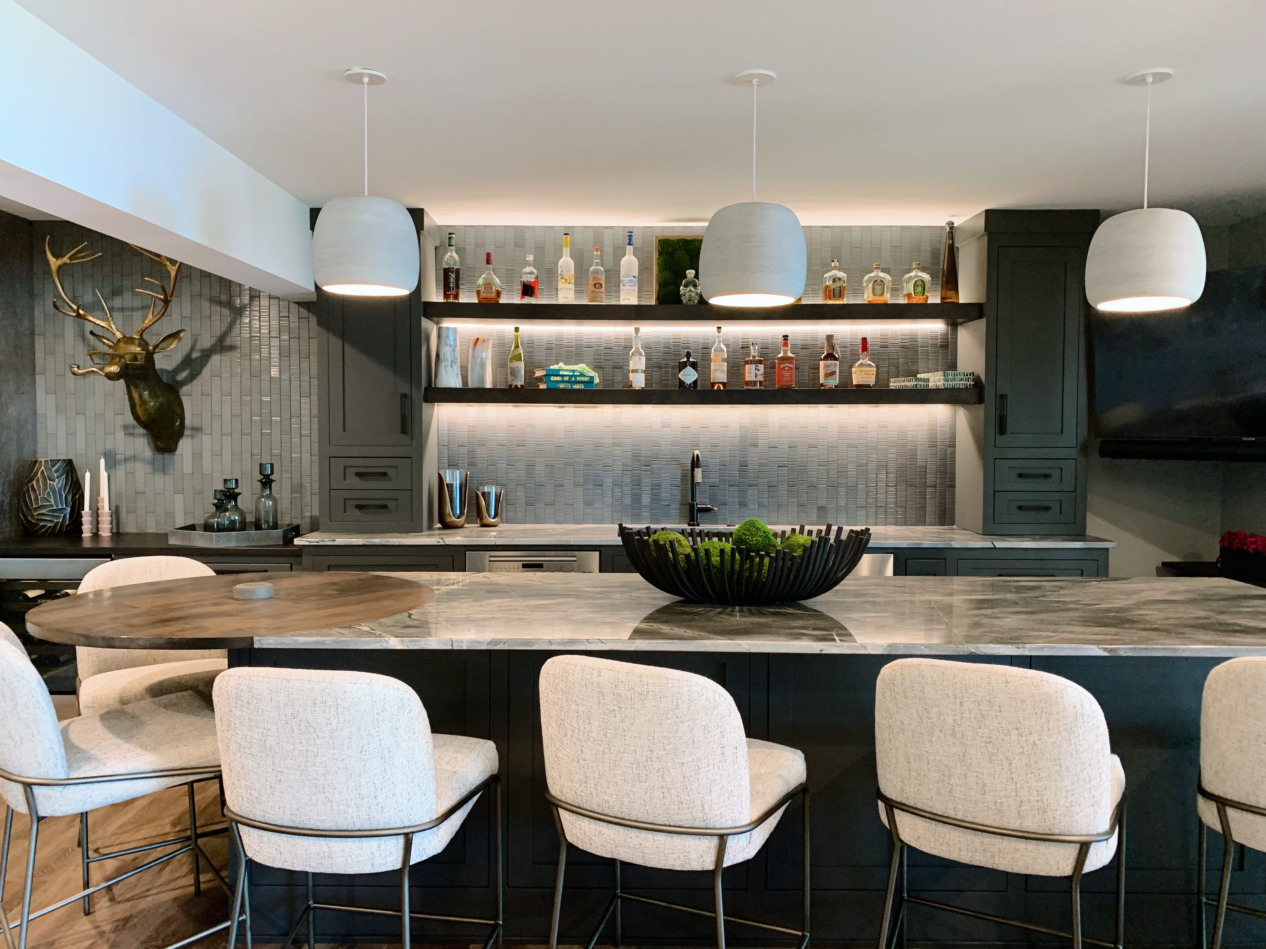 Custom wet bar with dark cabinetry, marble countertop, backlit open shelving, and brass stag wall sculpture — Mac & Morgan Interiors, Seneca SC