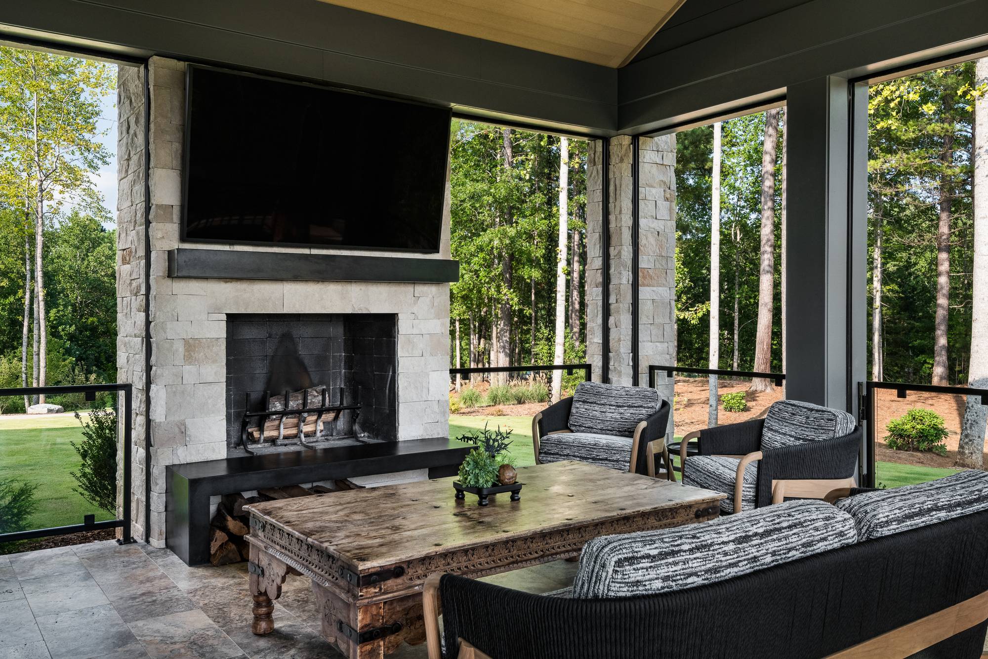 Covered outdoor living space with stacked stone fireplace and wooded views — Mac & Morgan Interiors, Upstate SC
