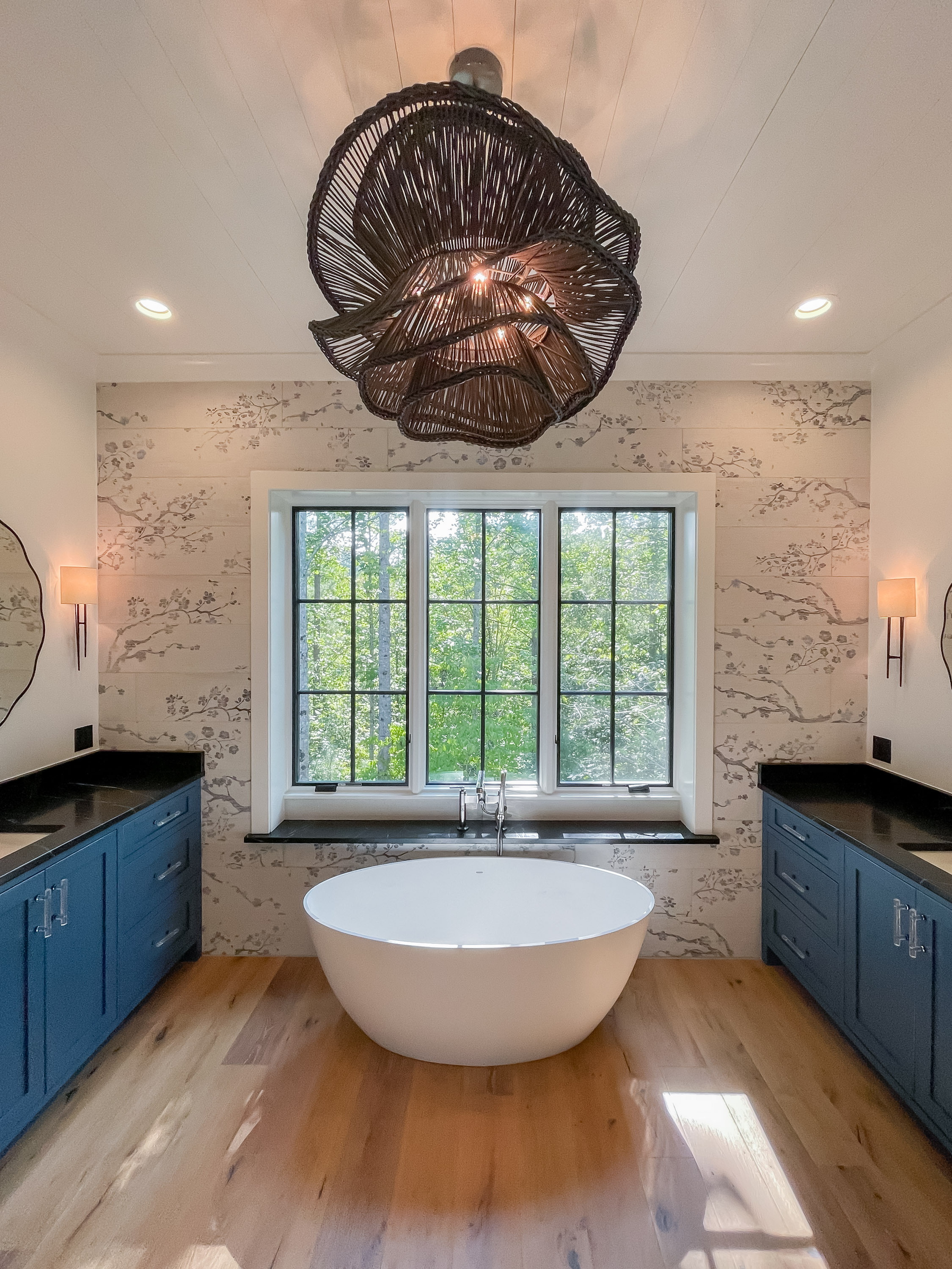 Luxury primary bathroom with freestanding soaking tub, navy vanity cabinets, botanical wallpaper, and sculptural chandelier — Mac & Morgan Interiors